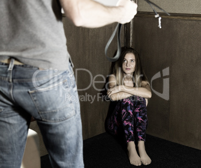 frightened woman sitting in the corner with a faceless man holding a belt, a conceptual shoot portraying the process and effects of domestic violence