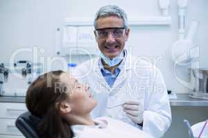 Smiling Dentist examining a patient with tools