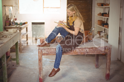 Beautiful female potter writing in notebook