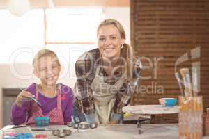 Smiling female potter and girl painting in pottery workshop