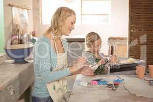 Female potter and girl painting in pottery workshop