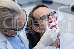 Female dentist examining male patient with tools