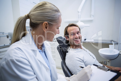 Female dentist writing on clipboard while interacting with male