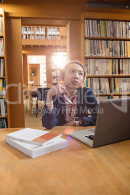 Thoughtful young woman using laptop in library