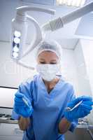 Dental assistant in surgical mask holding dental tools