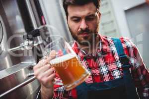 Manufacturer examining beer in glass by storage tank