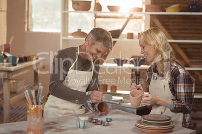 Smiling potters painting on cup