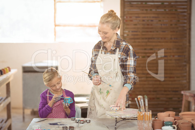 Female potter assisting girl in painting