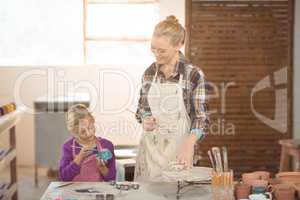 Female potter assisting girl in painting