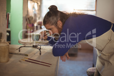 Attentive male potter painting on bowl