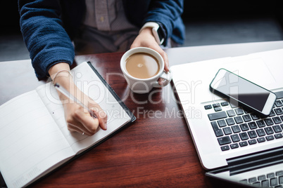 Woman writing in book while having tea