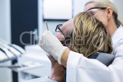 Female dentist examining male patient with tools