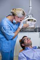 Smiling dentist assistant adjusting light over patients mouth