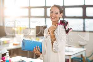 Female business executive holding exercise mat and shoes