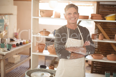Smiling male potter standing with arms crossed in pottery worksh
