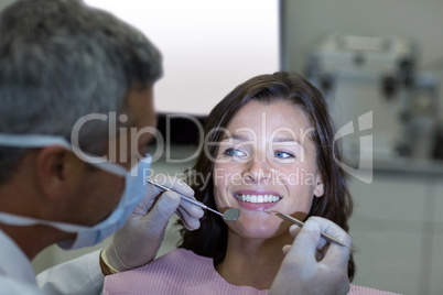 Dentist examining a female patient with tools