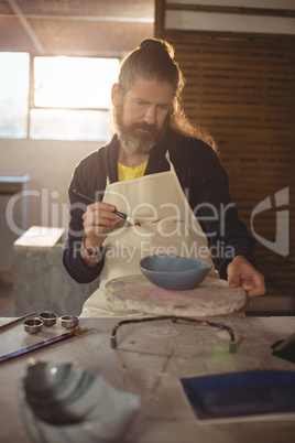 Attentive male potter painting on bowl