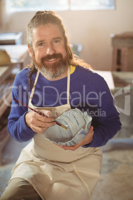 Smiling male potter painting on bowl