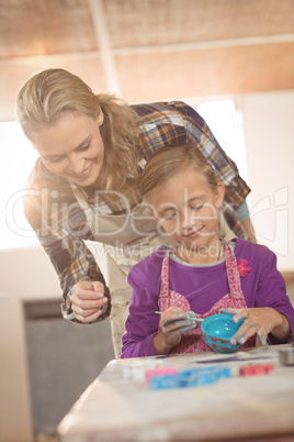 Female potter assisting girl in painting at pottery workshop