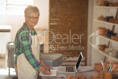 Portrait of female potter making note from laptop