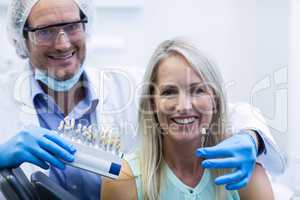 Dentist holding teeth shades while female patient smiling