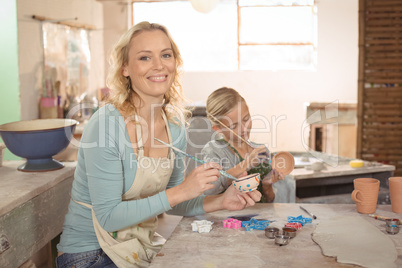 Female potter and girl painting in pottery workshop