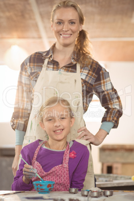 Female potter assisting girl in painting at pottery workshop
