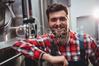 Smiling manufacturer standing by storage tank in brewery