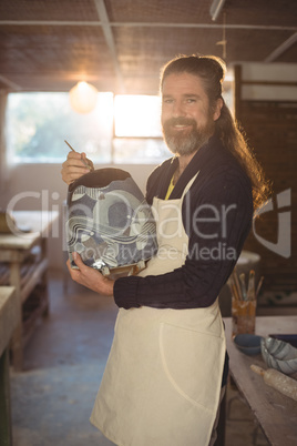 Smiling male potter painting on pot