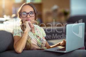 Thoughtful woman sitting on sofa and using laptop