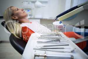 Woman relaxing on dentist chair with dental tools on foreground