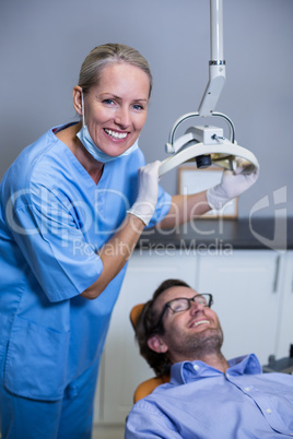 Smiling dentist assistant adjusting light over patients mouth