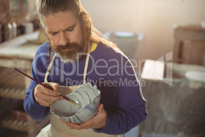 Attentive male potter painting on bowl