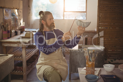 Attentive male potter painting on bowl