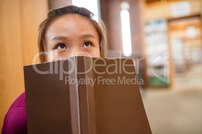 Thoughtful young woman covering her face with book