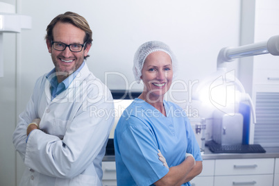 Smiling dentist and dental assistant standing with arms crossed