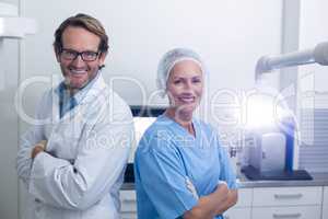 Smiling dentist and dental assistant standing with arms crossed
