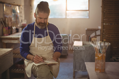 Male potter writing in notebook