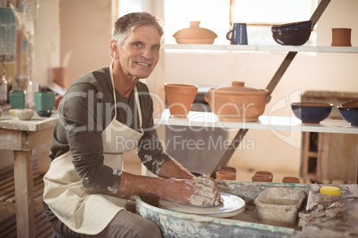 Smiling male potter making pot in pottery workshop