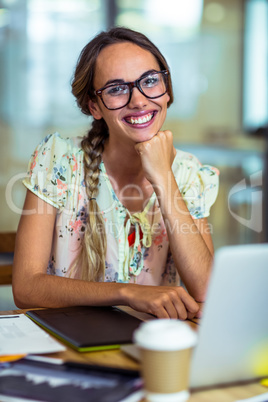 Smiling graphic designer sitting with hand on chin in office