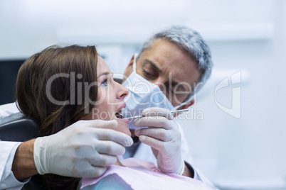 Dentist examining a female patient with tools
