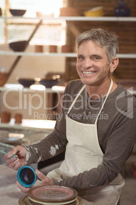 Smiling male potter painting on bowl