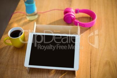Digital tablet, headphones and a cup of coffee on table