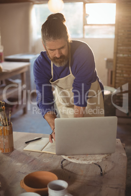 Male potter working on laptop