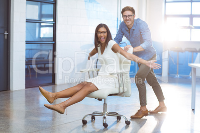 Business executive pushing businesswoman in office chair