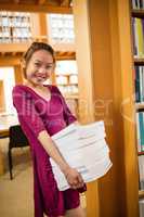 Portrait of young woman holding stack of books in library