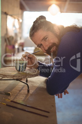 Smiling male potter painting on bowl