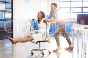 Business executive pushing businesswoman in office chair