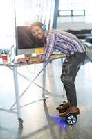 Smiling man standing on hoverboard and using laptop in office