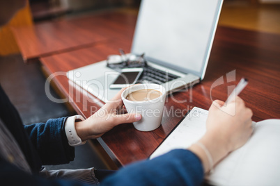 Woman writing in book while having tea